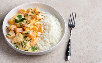 Bowl of pumpkin in sour cream sauce with rice sprinkled with fresh parsley on beige textured stone table, top view, copy space. Vegetarian food