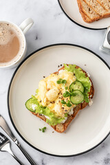 Scrambled eggs on grilled toast with salad leaves, cheese and micro greens on plate on white marble background close up top view. Delicious healthy breakfast