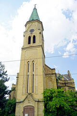 Fototapeta premium Architectural gems of Vojvodina: Evangelical Church, landmark of Pancevo. View of the tall square bell tower made of yellow brick with rusty clock face and Gothic decor. Travel to Serbia.