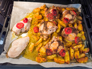 Chicken and potatoes roasting in the oven with cherry tomatoes and spices