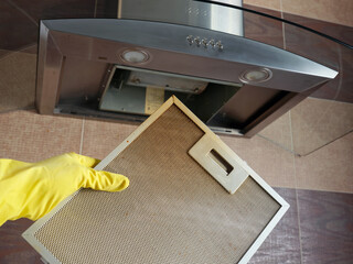 Female hand in protective yellow rubber glove holds dirty kitchen hood panel.
