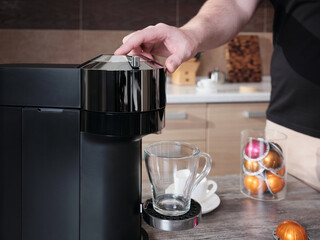 Early in the morning, a man makes coffee in a capsule coffee machine in his home kitchen.
