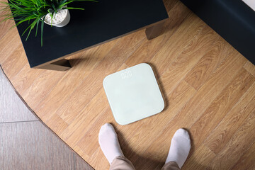 Top view a woman stands in front of an electronic scale for weighing a person, hesitant.