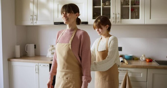 Girl ties her mother apron behind her back while cooking and baking at home in the kitchen. Teamwork mother and daughter in the kitchen