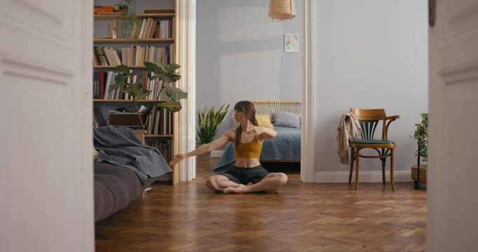 Girl in yellow top sits on floor and creates classical dance elements with hands during dance improvisation at home. Dance improvisation and dancing at home