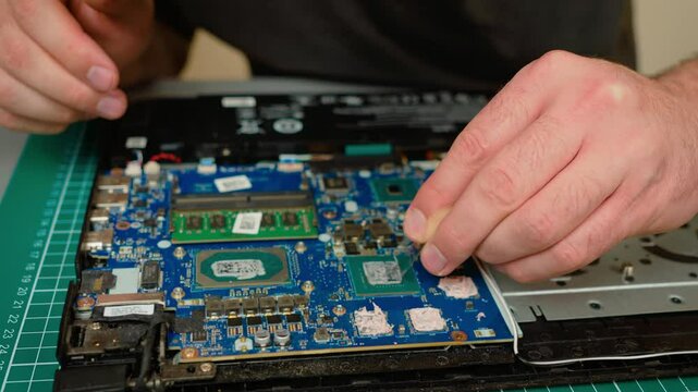 Cleaning old thermal paste from graphics chip in laptop motherboard. Removing dried compound from GPU surface for maintenance. Preparing chip by wiping thermal residue for new paste application