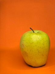 Green apple on a orange background, close-up, selective focus
