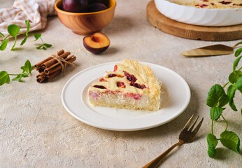 Sliced ​​Kataifi dough pie with curd filling and plums on a white plate on a light concrete background. Plum recipes.
