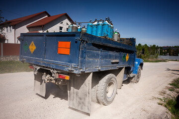 Obraz premium Blue cargo truck carrying gas cylinders on rural road under clear sky