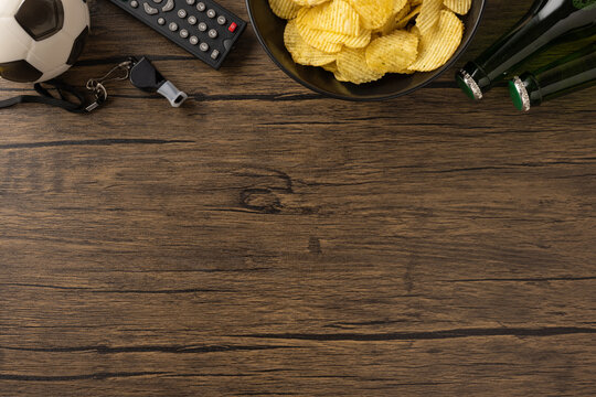 Football viewing setup with chips, beer, and sports items, arranged on a wooden table