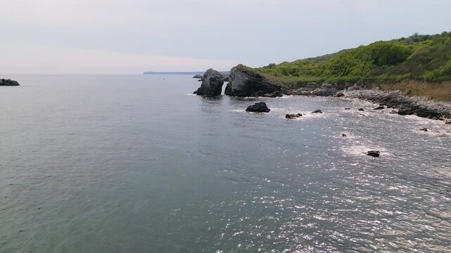 Aerial view of Yaylata nature area near Rusalka village on the Black Sea coast of Bulgaria. Rocky cliffs, turquoise water, and lush green hills create a dramatic and wild coastal scene