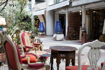 Ornate antique chairs and a carved wooden table in a sunlit courtyard shop, creating a charming and inviting atmosphere.