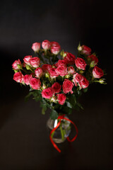 Beautiful bouquet of pink (red) roses bushes with water drops on a black background. Selective focus, close-up.