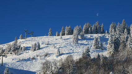Fototapeta na wymiar Stunning winter landscape photo of a ski resort in the mountains with snow-covered trees and a clear blue sky. Perfect for winter travel and tourism.