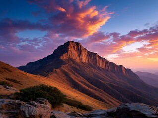Fototapeta premium Mountain peak illuminated by sunset with cloudy sky. Grassy slopes in the foreground