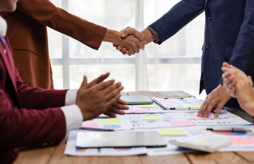 Business people shaking hands after successful meeting. Two business people shaking hands while their colleagues are clapping, after reaching an agreement during a productive meeting.