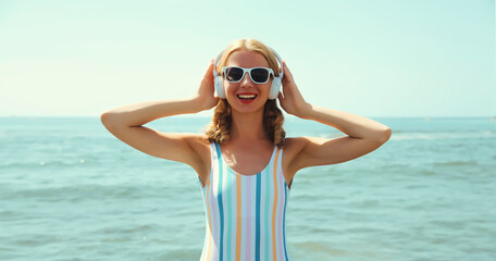 Summer portrait happy young woman smiles enjoys listening to music with headphones on beach at sea