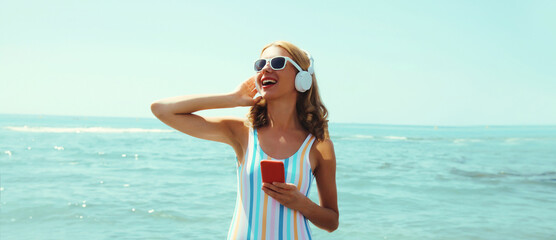 Summer portrait happy young woman smiles enjoys listening to music with headphones on beach at sea