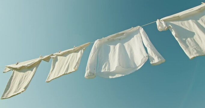 Freshly washed white clothes fluttering in the wind on a clothesline under bright blue sky in sunny weather