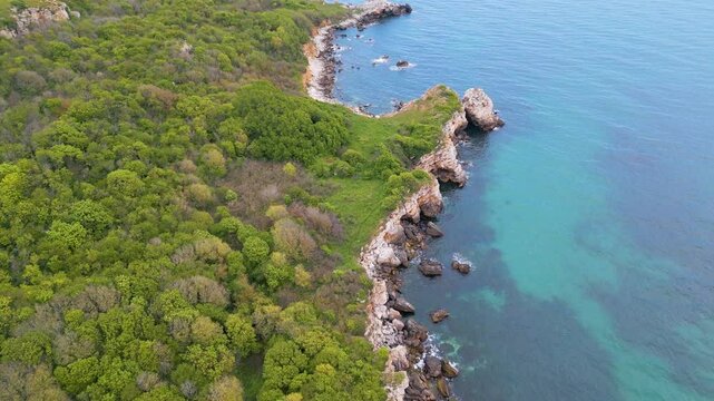 Aerial view of Yaylata nature area near Rusalka village on the Black Sea coast of Bulgaria. Rocky cliffs, turquoise water, and lush green hills create a dramatic and wild coastal scene