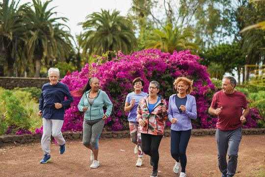 Happy senior people running together at city park - Group of elderly multiracial friends doing sport outdoor - Healthy lifestyle and support concept