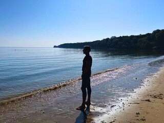 Slim man in jeans and top and bare feet on sandy Studland beach looking out to Old Harry Rock in Dorset UK.