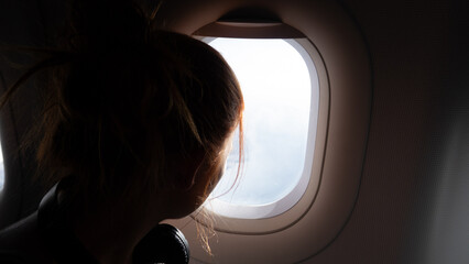 Silhouette of a woman gazing out the airplane window at the clouds.
