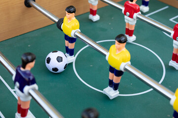 A close-up shot of a foosball game in progress. The focus is on the players and the ball.