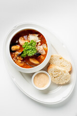 A gourmet seafood soup with mussels, shrimp, and fish, garnished with fresh parsley, served with crusty bread and creamy sauce on a white plate.