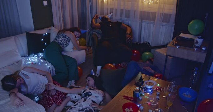 Friends passed out after a birthday party at someone's home. They are sleeping on a white couch and floor surrounded by party favors and drinks.