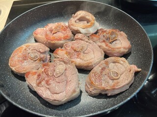 Fresh raw meat shanks roasting in smoking hot frying pan on electric stove top. Close-up top view of fried turkey steaks cooking for delicious meal , home cooking.