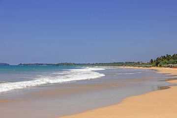 Wide sandy beach panorama with blue sky and tropical coastline