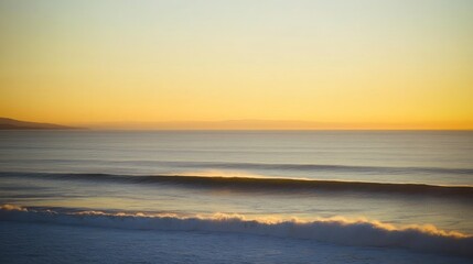 Serene sunset over calm ocean waves with distant mountains and soft golden hues in the sky