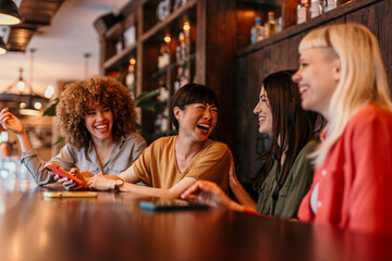 Four young women laughing and talking in a bar