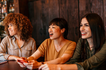 Multi-ethnic group of women laughing and having fun at a bar, one holding a cell phone