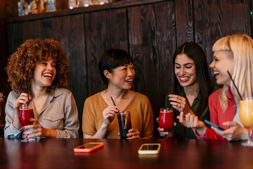 Four female friends enjoying drinks and conversation at a bar