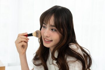 Beautiful teenage girl using blusher to apply makeup in front of a mirror at home.