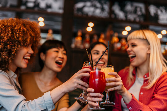 Cheerful female friends toasting cocktails at bar counter