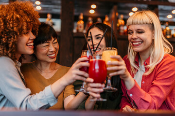 Cheerful female friends toasting cocktails in bar