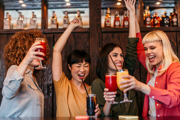 Cheerful female friends raising cocktails and having fun at bar counter