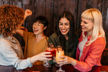 Four female friends toasting cocktails at bar counter