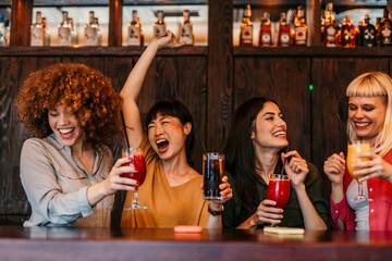 Cheerful multi-ethnic girlfriends drinking cocktails at the bar counter
