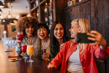 Cheerful friends taking selfie and drinking cocktails at the bar counter