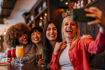 Four women taking a selfie while enjoying drinks at the bar