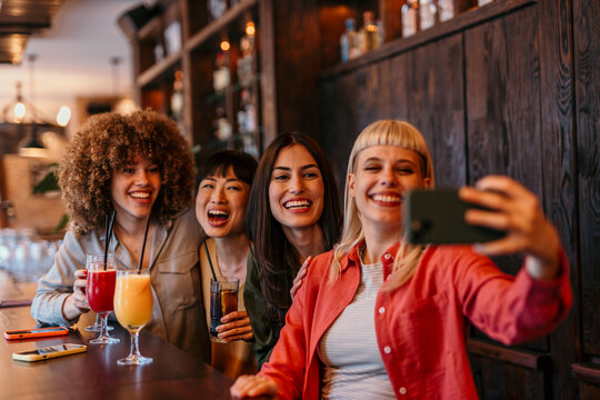 Cheerful friends taking selfie while drinking cocktails at bar counter