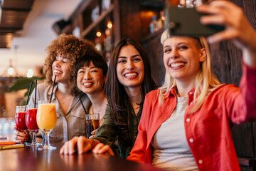 Four happy female friends taking selfie in bar while drinking cocktails