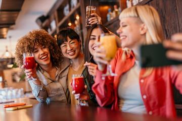 Cheerful multi-ethnic friends taking selfie while drinking cocktails at bar counter