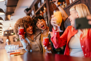 Happy women taking a selfie with cocktails at the bar counter