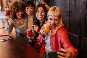 Cheerful friends taking selfie while drinking cocktails at the bar