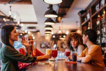 Cheerful female friends enjoying cocktails and conversation at bar counter